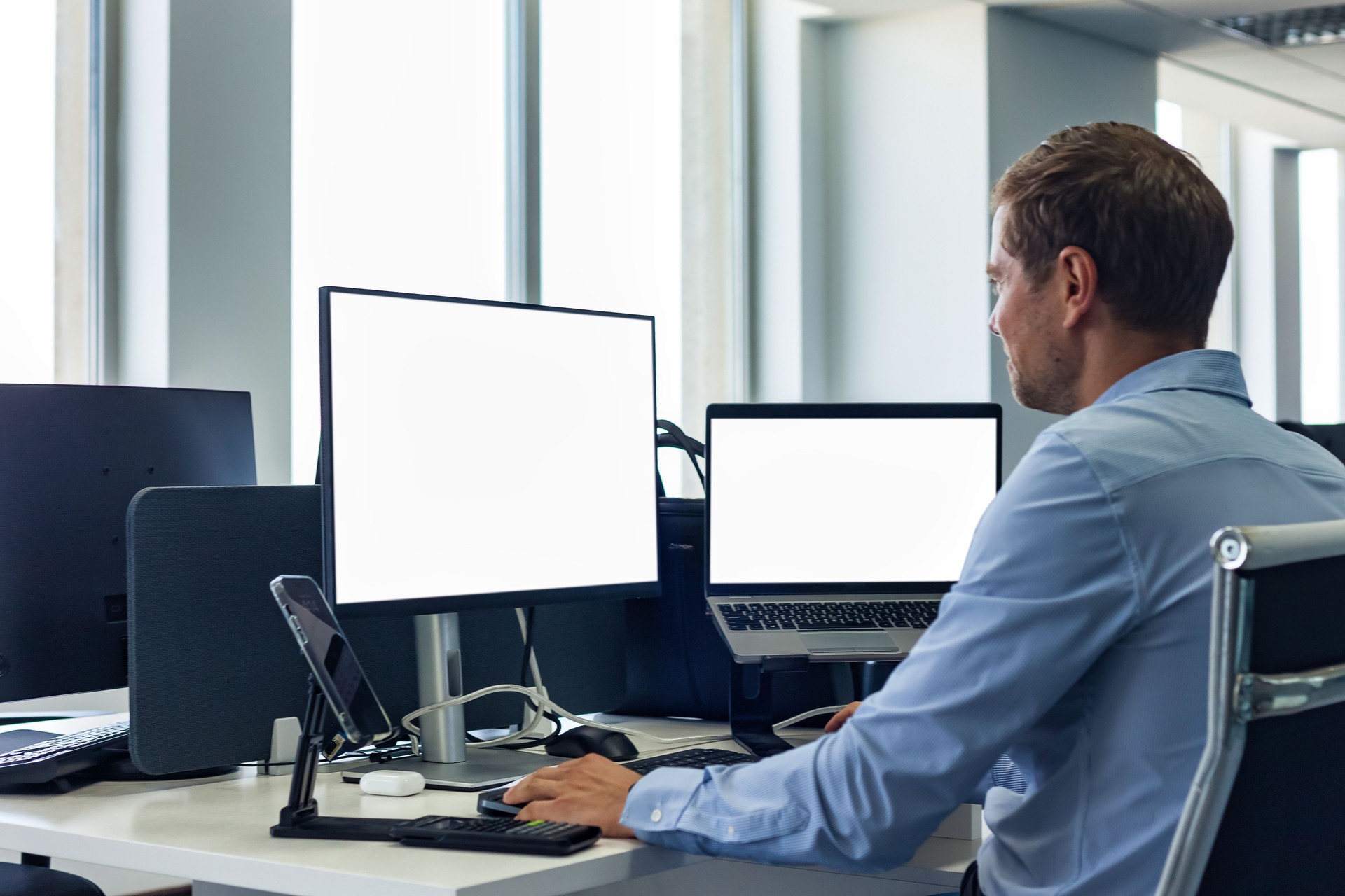 From behind male manager businessman in blue shirt works in corporate office. Man broker agent using pc computer at desk, rear view. Business development growth, solutions concept. Copy ad text space